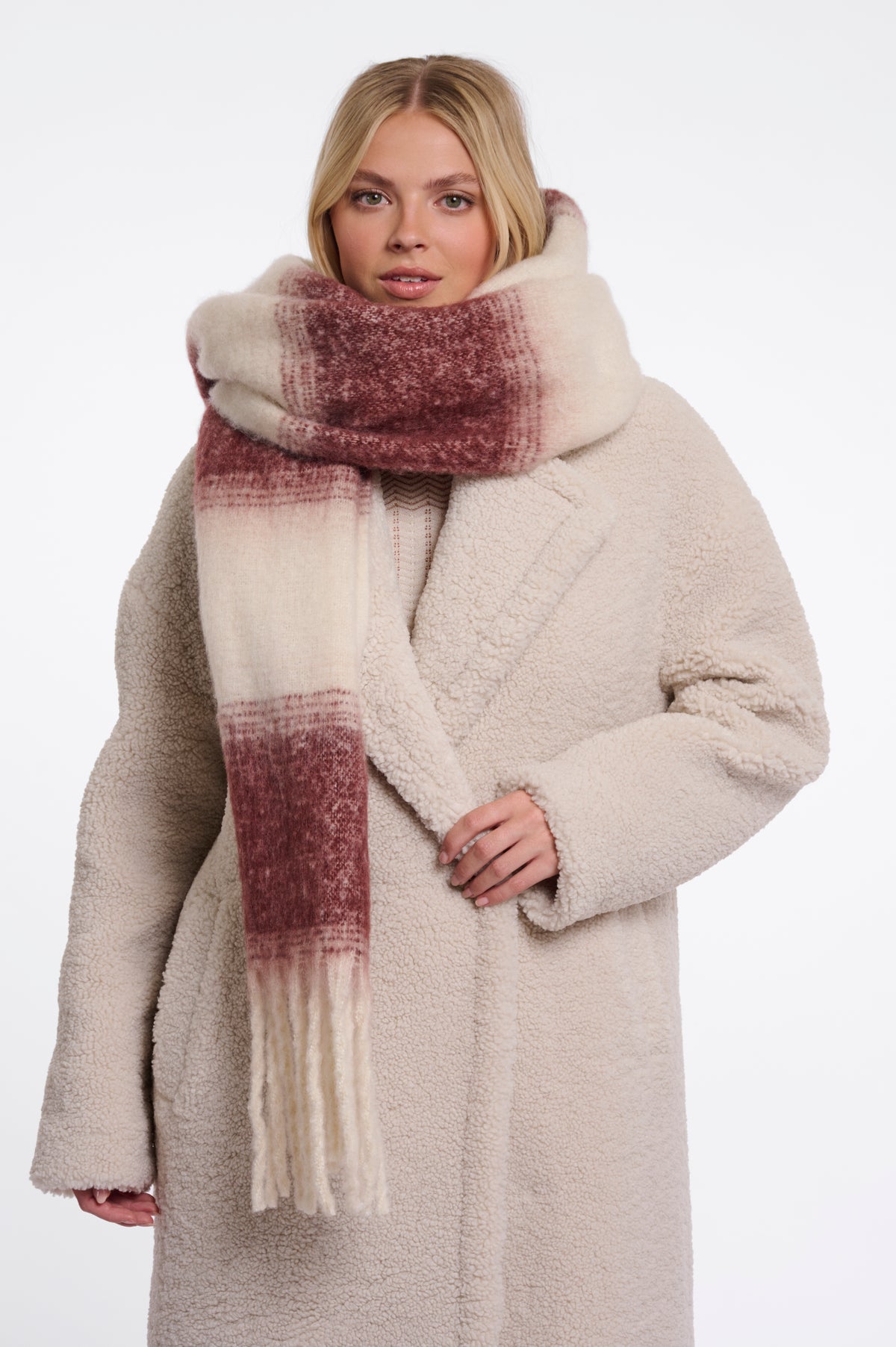 Woman wearing a beige coat and plaid scarf on a white background