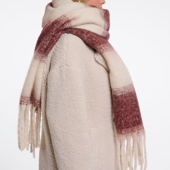 A woman shown from the back wearing a thick cream-colored teddy coat and a matching fringed scarf with a dusty rose gradient.