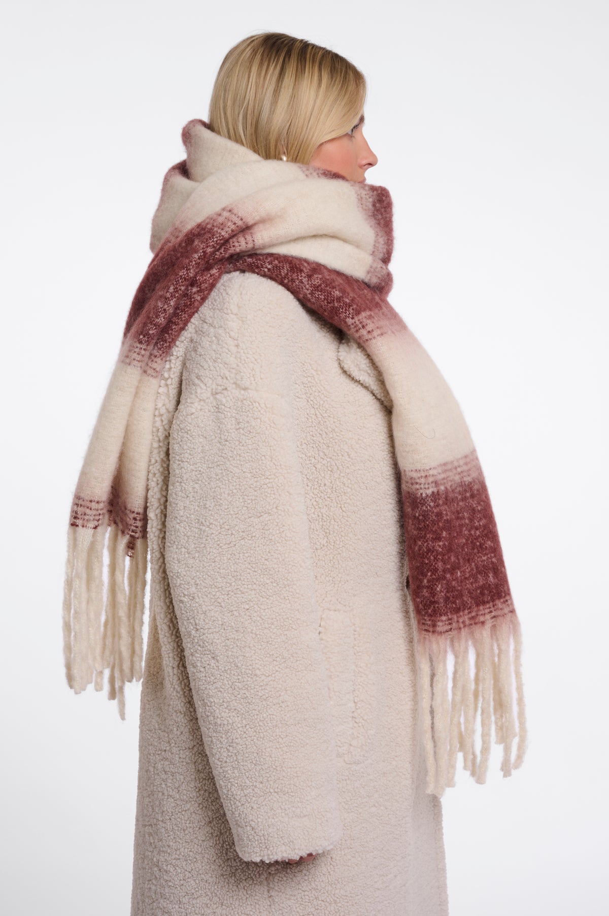 A woman shown from the back wearing a thick cream-colored teddy coat and a matching fringed scarf with a dusty rose gradient.