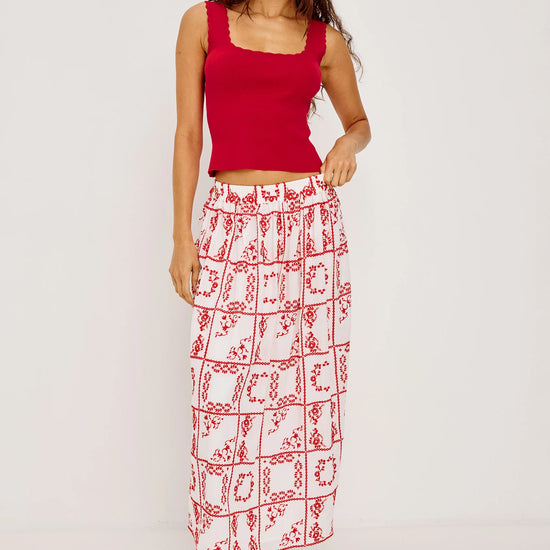Woman wearing a red top and patterned skirt on a white from background from rails