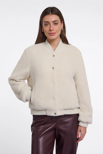 A woman modeling a cream-colored, fuzzy button-up cardigan sweater paired with dark brown faux-leather pants, shot against a plain white studio background.