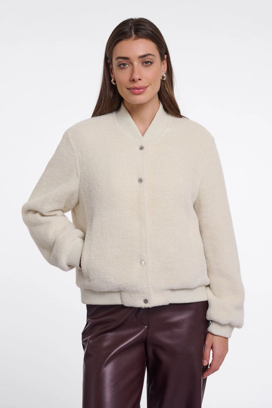 A woman modeling a cream-colored, fuzzy button-up cardigan sweater paired with dark brown faux-leather pants, shot against a plain white studio background.