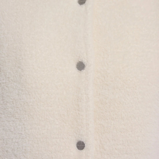 Close-up of a cream-colored fuzzy cardigan with dark gray buttons, showing the soft texture and collar.