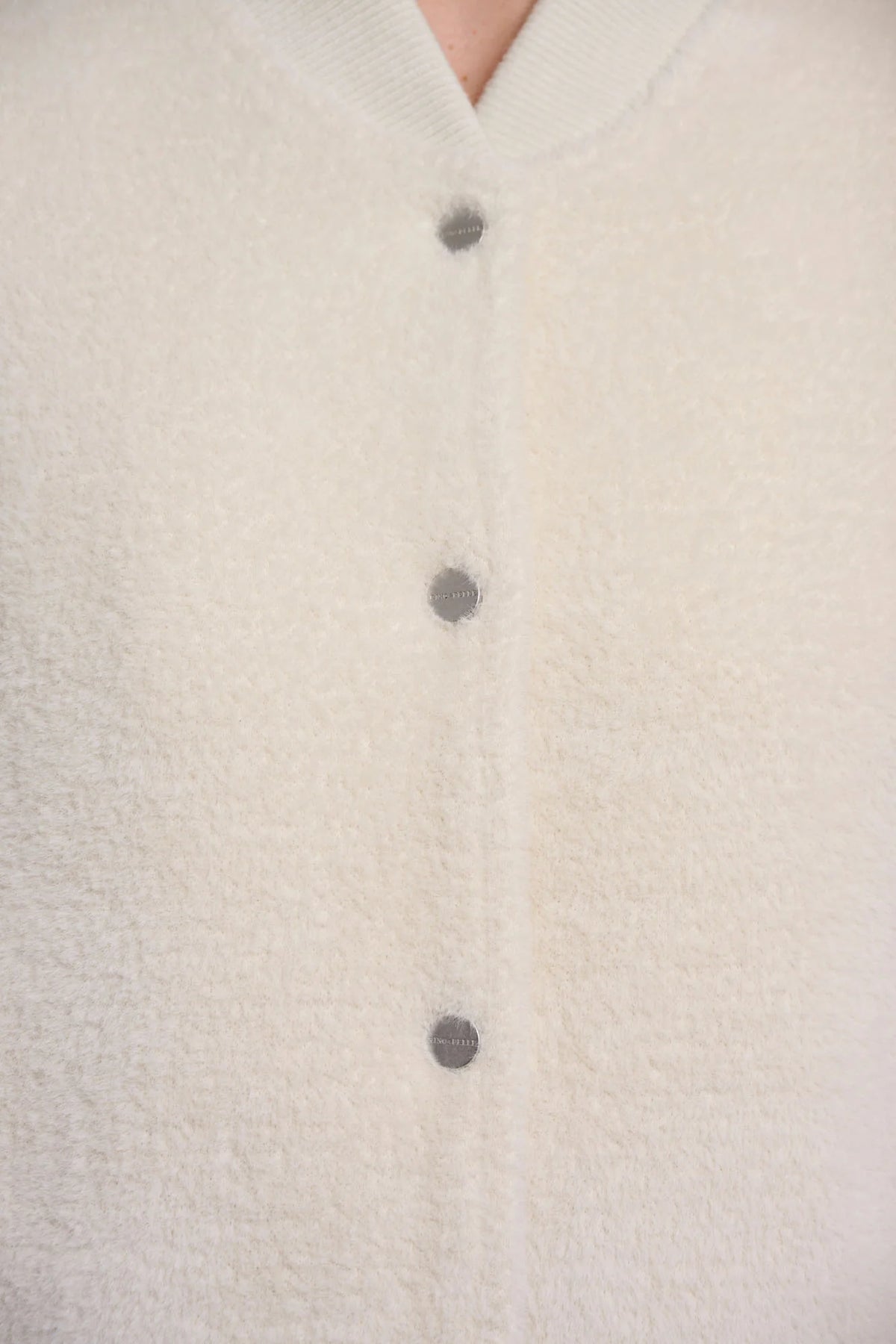 Close-up of a cream-colored fuzzy cardigan with dark gray buttons, showing the soft texture and collar.