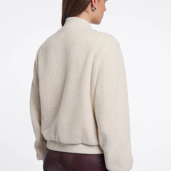 Person wearing a beige sweater and dark pants on a white background