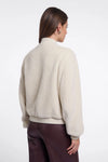 Person wearing a beige sweater and dark pants on a white background