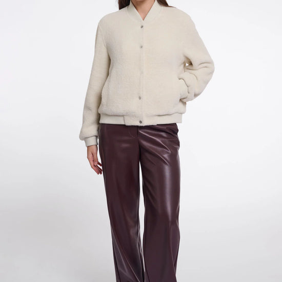A woman modeling a cream-colored fuzzy button-up cardigan paired with dark brown wide-leg faux leather pants, set against a plain light gray studio background.