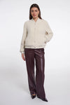A woman modeling a cream-colored fuzzy button-up cardigan paired with dark brown wide-leg faux leather pants, set against a plain light gray studio background.
