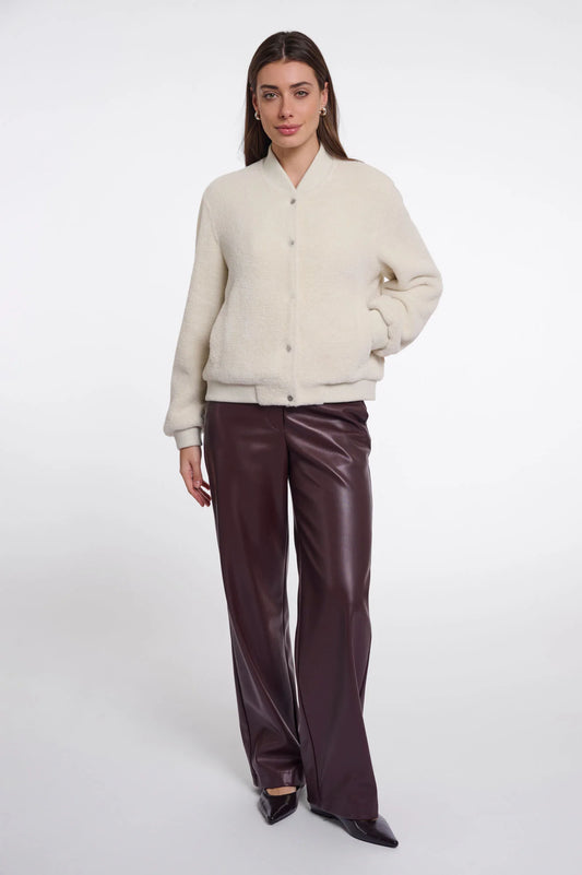 A woman modeling a cream-colored fuzzy button-up cardigan paired with dark brown wide-leg faux leather pants, set against a plain light gray studio background.