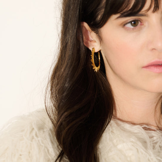 large gold hoop earrings with varying sized spike detailing along the edging with butterfly fastening from rachel jackson model shot