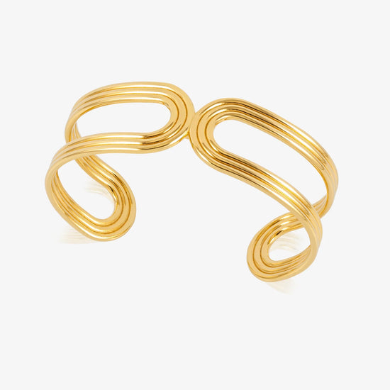 A gold-toned metal cuff bracelet with a modern, wavy, multi-layered loop design, shown on a clean white background.