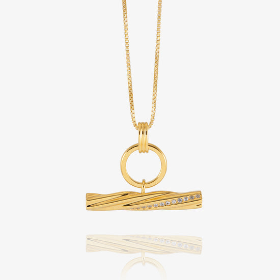 A gold pendant necklace featuring a twisted bar design with a row of small clear stones, suspended from a delicate gold chain against a light gray background.
