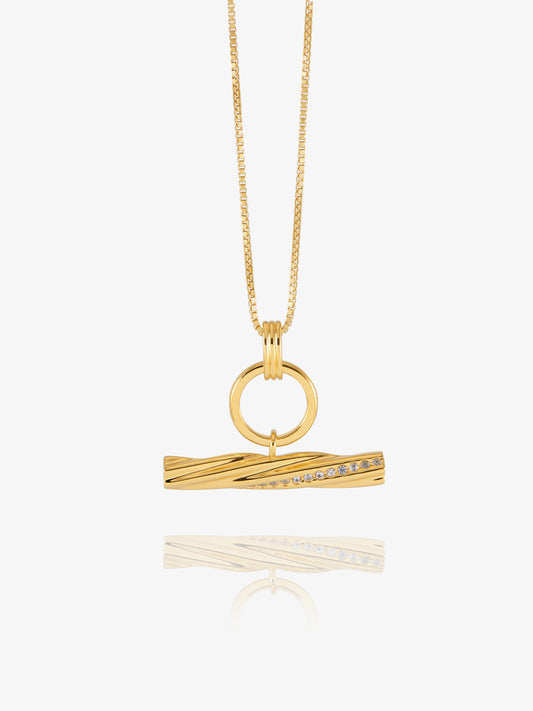 A gold pendant necklace featuring a twisted bar design with a row of small clear stones, suspended from a delicate gold chain against a light gray background.