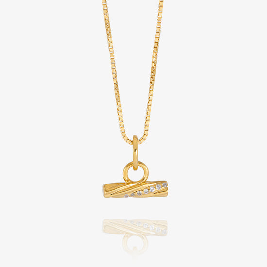 A gold chain necklace with a small horizontal bar pendant featuring a row of clear stones, displayed against a light gray background with a soft reflection below.