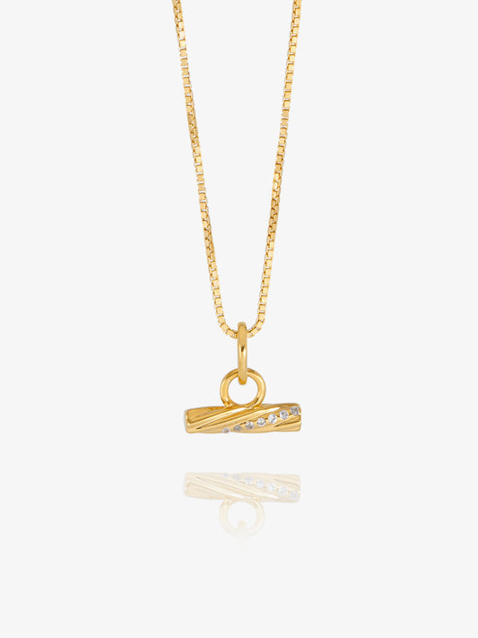 A gold chain necklace with a small horizontal bar pendant featuring a row of clear stones, displayed against a light gray background with a soft reflection below.