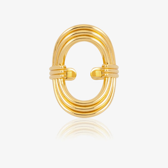 A gold-toned metal ring with a multi-strand oval design and a twisted center detail, shown on a clean white background with a soft reflection below.