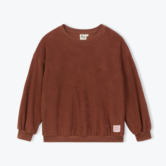 A brown long-sleeve crewneck sweatshirt with a small pink brand tag on the lower right hem, displayed flat against a light gray background.