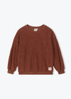 A brown long-sleeve crewneck sweatshirt with a small pink brand tag on the lower right hem, displayed flat against a light gray background.