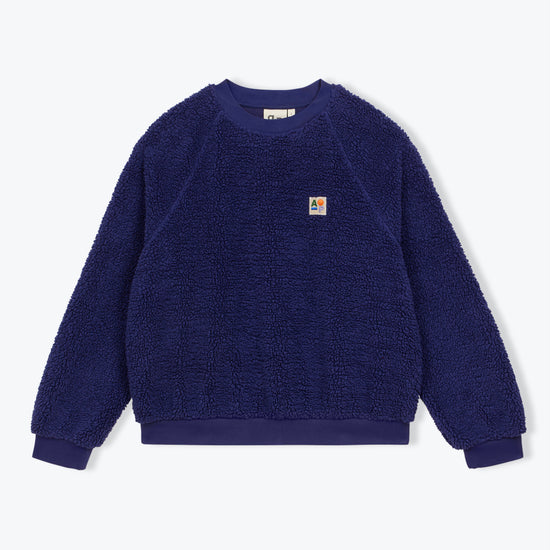 A dark blue sherpa fleece crewneck sweatshirt with a small Carhartt logo patch on the left chest, displayed flat against a light gray background.