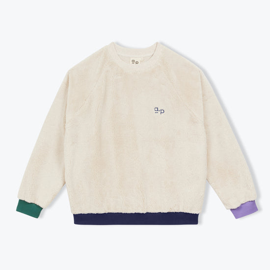 A cream-colored fuzzy crewneck sweatshirt with a small embroidered 'ap' logo on the chest, featuring contrasting green, navy, and purple ribbed cuffs and hem.