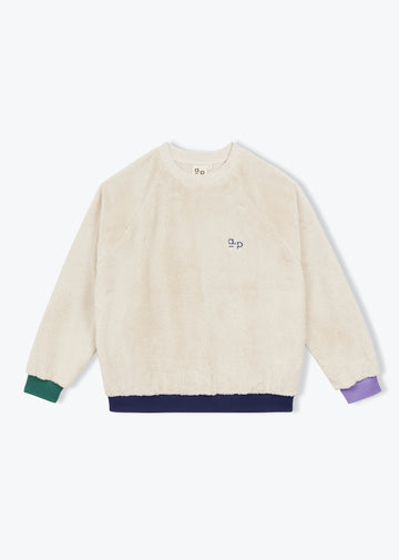 A cream-colored fuzzy crewneck sweatshirt with a small embroidered 'ap' logo on the chest, featuring contrasting green, navy, and purple ribbed cuffs and hem.