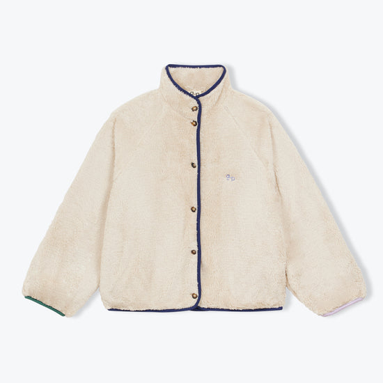 A cream-colored sherpa jacket with dark navy blue trim along the collar, front buttons, cuffs, and hem, featuring a small embroidered logo on the left chest.