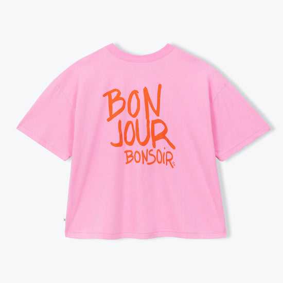 A pink short-sleeve t-shirt with orange text on the back reading 'BON JOUR BONSOIR', displayed against a clean white background.