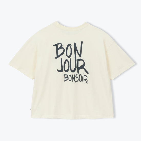 An off-white short-sleeve t-shirt with 'BON JOUR BONSOIR' printed in black across the back, displayed on a clean white background.