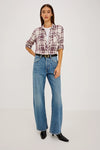 A woman wearing a long-sleeve plaid button-up shirt in cream and burgundy, tucked into blue jeans with a black belt.