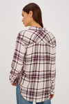 A woman wearing a long-sleeve plaid button-up shirt in cream and burgundy, tucked into blue jeans with a black belt.