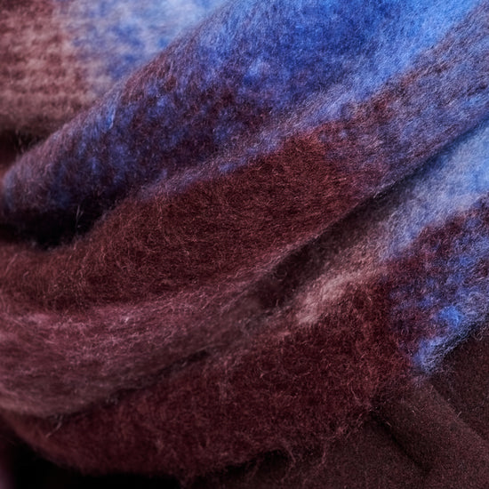 A close-up of a soft, fuzzy scarf or fabric with layered plaid stripes in blue, burgundy, and dark brown.