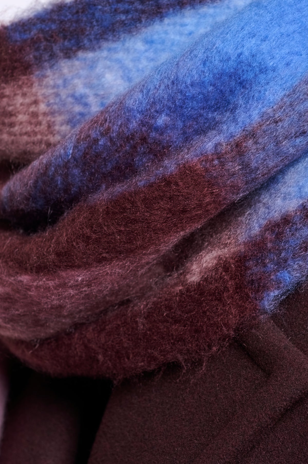 A close-up of a soft, fuzzy scarf or fabric with layered plaid stripes in blue, burgundy, and dark brown.