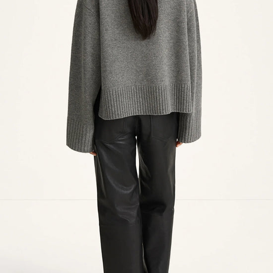 Person wearing a gray sweater and black pants on a white background