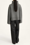 Person wearing a gray sweater and black pants on a white background