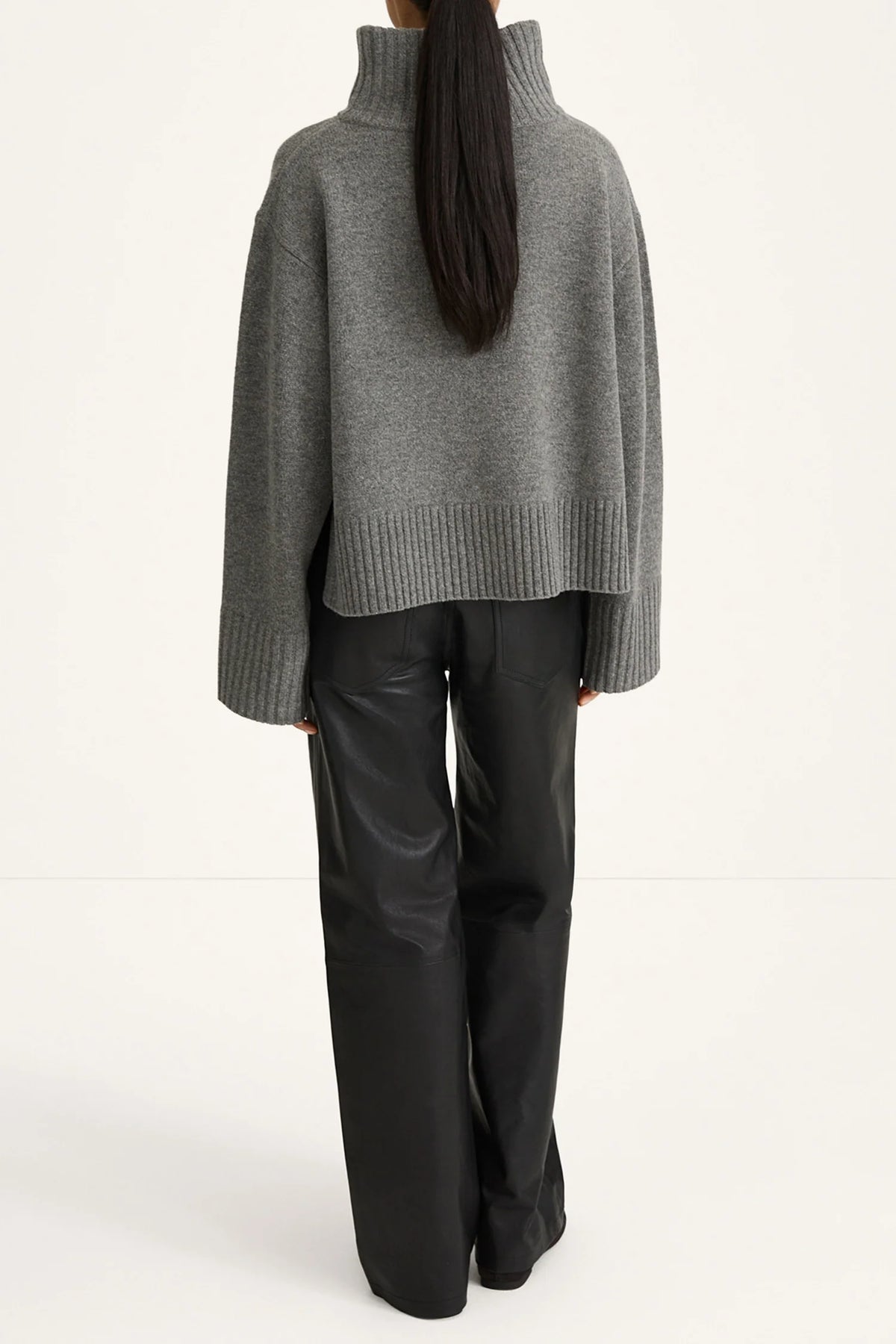 Person wearing a gray sweater and black pants on a white background