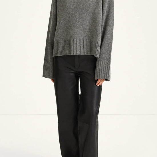 A model wearing a gray ribbed turtleneck sweater and black wide-leg trousers, standing against a plain white studio background.