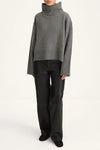 A model wearing a gray ribbed turtleneck sweater and black wide-leg trousers, standing against a plain white studio background.