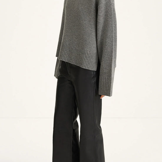A model shown from the side wearing a gray ribbed turtleneck sweater and black wide-leg trousers against a plain white studio background.