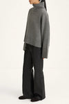 A model shown from the side wearing a gray ribbed turtleneck sweater and black wide-leg trousers against a plain white studio background.