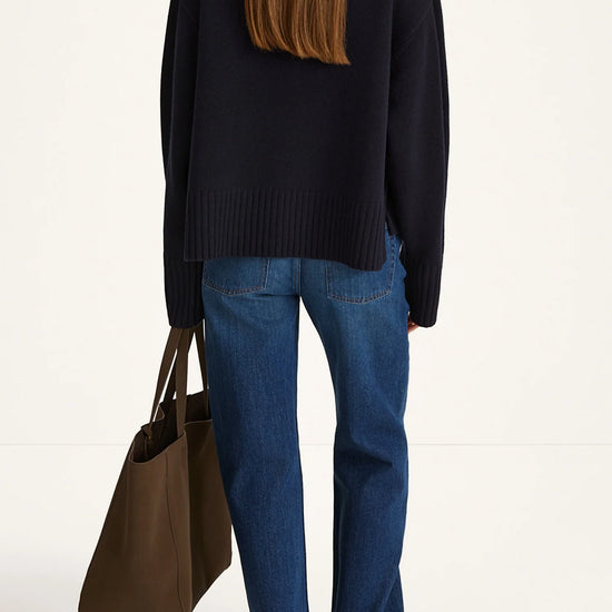Person wearing a black sweater and blue jeans holding a brown bag on a white background