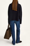 Person wearing a black sweater and blue jeans holding a brown bag on a white background