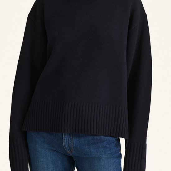 Person wearing a black turtleneck sweater and blue jeans on a white background