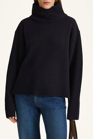 Person wearing a black turtleneck sweater and blue jeans on a white background