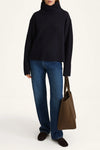 Person wearing a black turtleneck sweater, blue jeans, and holding a brown bag on a white background