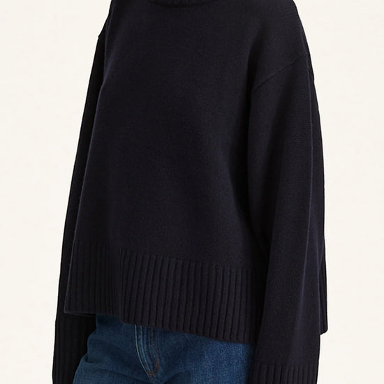 Person wearing a black turtleneck sweater and blue jeans on a white background