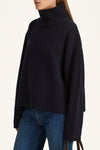 Person wearing a black turtleneck sweater and blue jeans on a white background