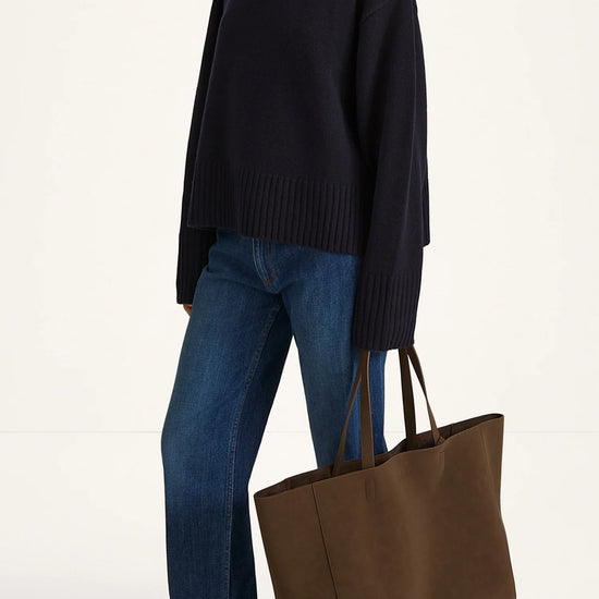 Person wearing a black sweater and blue jeans holding a brown tote bag on a white background