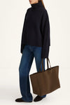 Person wearing a black sweater and blue jeans holding a brown tote bag on a white background