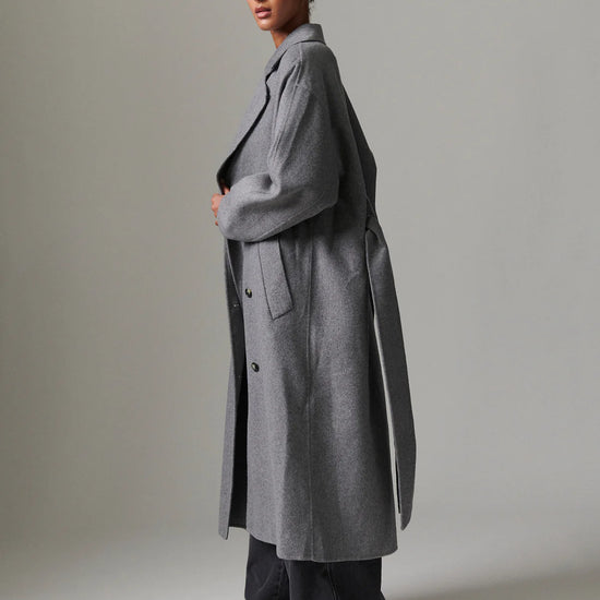 Woman wearing a long gray coat against a plain background