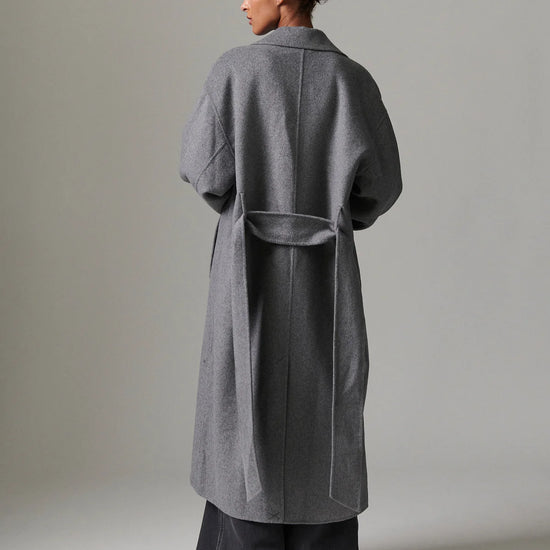 Person wearing a gray coat against a plain background